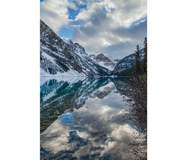 A perfect reflection of the snowy mountainsides and cloudy blue sky upon the still turquoise waters of Lake Louise in Alberta 