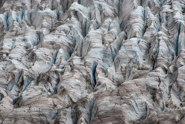 A rugged glacier, dotted with brown lines and deep cracks and crags. 