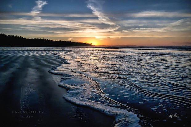 Tide coming into a soft, sandy beach at sunset, with streaks of cloud along a deep blue sky. 