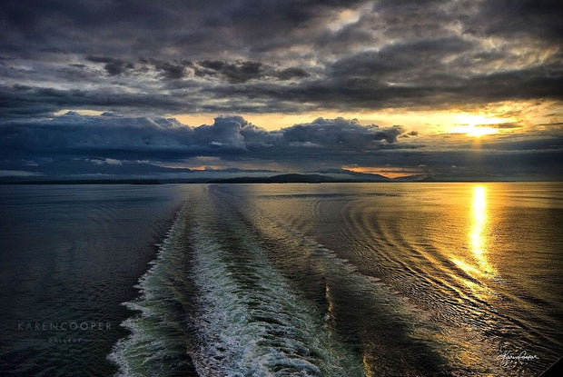 The wake of a ferry below a cloudy sky at sunset in the ocean