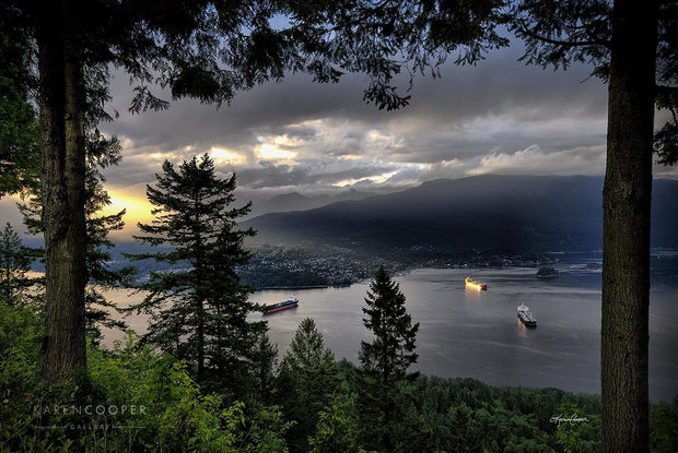 Fine art luxury nature landscape contemporary photography by Karen Cooper Gallery A stormy sky hangs over the Burrard Inlet, with three transport ships waiting in the waters. Golden sun rays shine upon one of the vessels in Vancouver British Columbia Canada 